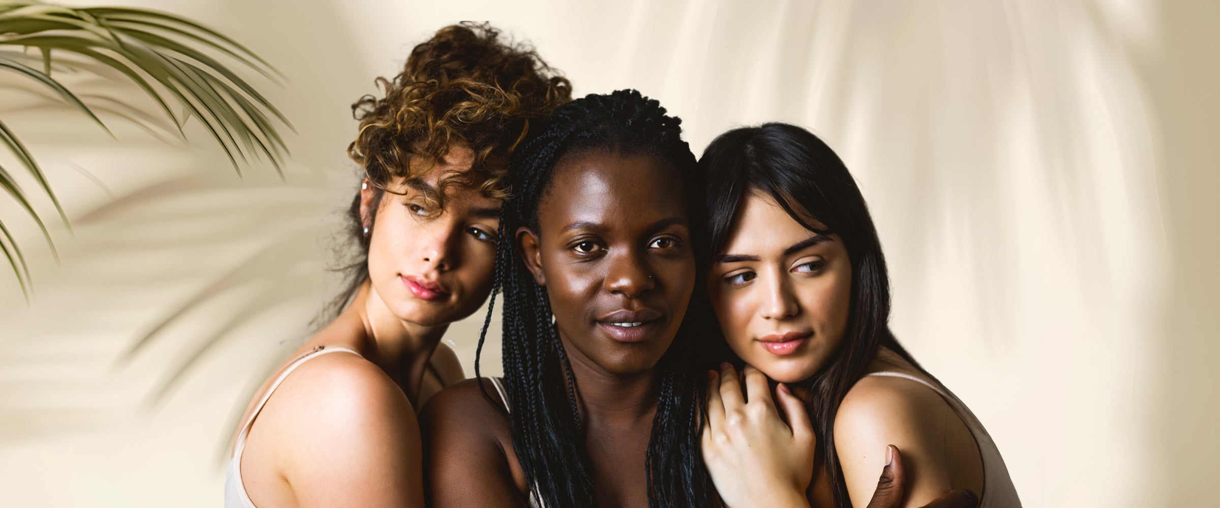 Multicural group of three women standing close together against a neutral background represents all hair types.