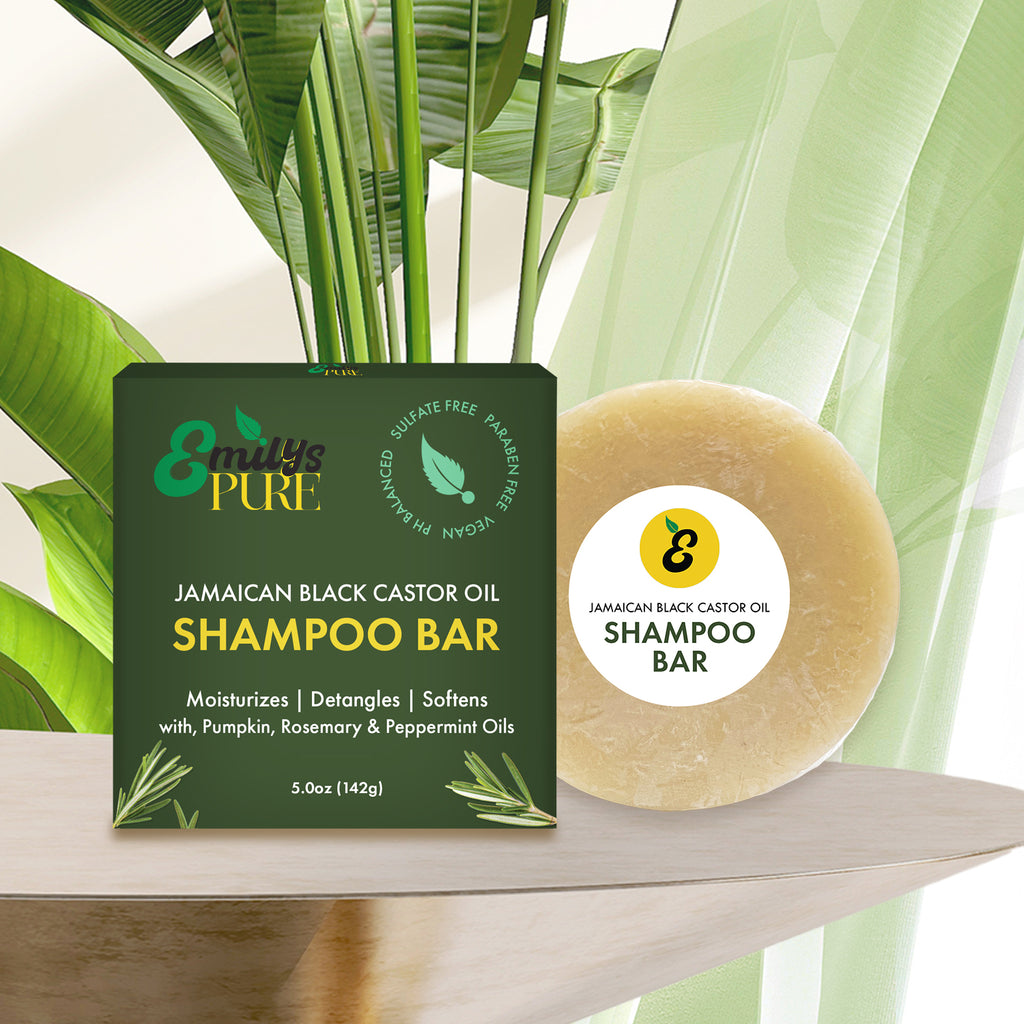 Emily's Pure Jamaican Black Castor Oil Shampoo Bar packaged on a wooden surface with plants in the background. 